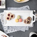 A white rectangular porcelain platter with black circles on the handles holding a plate of cookies and tea.