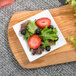 A table with a white square porcelain 10 Strawberry Street tid bit tray holding a salad with strawberries and blueberries.