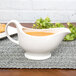 A white 10 Strawberry Street Whittier gravy boat on a table with brown liquid in it.
