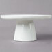 A white 10 Strawberry Street Whittier porcelain cake stand on a gray surface.