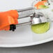A Vollrath orange squeeze handle disher on a plate with a sushi roll.