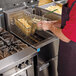 A man in a red shirt and black apron using a Frymaster natural gas floor fryer to cook french fries.