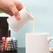 A person pouring milk from a Tuxton eggshell white creamer into a white mug.