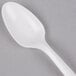 A Dart white plastic teaspoon on a gray surface.