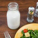 An American Metalcraft glass milk bottle next to a plate of salad.