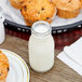 An American Metalcraft glass milk bottle next to muffins on a table.