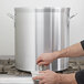 A hand pouring water into a large Vollrath Wear-Ever aluminum stock pot.