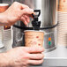 A person pouring coffee from a Town water boiler into a cup.