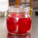 An American Metalcraft condiment mason jar filled with red liquid and cherries on a counter.