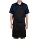A man wearing a black Chef Revival bib apron with his hands on his hips.