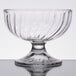 An Arcoroc clear glass dessert dish with a curved base on a table.