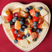A Eco-gecko heart-shaped palm leaf plate filled with fruit on a red surface.