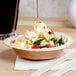 A bowl of pasta with vegetables and cheese in a Eco-gecko palm leaf bowl on a table.