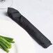 A fork wrapped in a black Hoffmaster linen-feel dinner napkin next to a plate of green beans.
