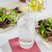A glass of water with ice next to a plate of salad.