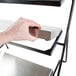 A hand holding a Tablecraft CaterWare three-tiered metal display stand with cooling plates.