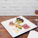 A Tablecraft white square melamine tray with a plate of food and wine on a table.
