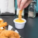 A person dipping a piece of breaded food into a white Carlisle ramekin.
