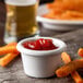 A white Carlisle ramekin filled with ketchup next to a bowl of french fries on a table.