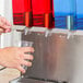 A person pouring water into a plastic cup from a Crathco stainless steel cold beverage dispenser.