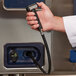 A hand holding a black hose in front of an Alto-Shaam Combitherm Proformance electric combi oven.
