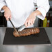 A chef cutting a piece of meat on a black resin grooved cutting board.