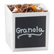 A white square container with a black sign reading "Granola" on it filled with brown granola.