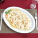 A white oval melamine platter with pasta, shrimp, and sauce on it.