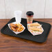 A Carlisle black Glasteel tray with hot dogs, french fries, and a drink on a table.