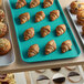 A green Cambro market tray of croissants and muffins on a bakery display counter.