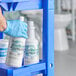 A person in blue gloves holding a white bottle of Noble Chemical Non-Valient toilet bowl cleaner.