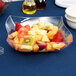 A clear Fineline plastic bowl filled with fruit salad on a table.
