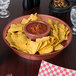 A round paprika deli server filled with chips and salsa on a table.