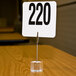 An American Metalcraft acrylic alligator clip card holder with a number on a table.