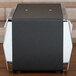 A black Vollrath Minifold napkin dispenser with silver metal accents on a wooden table.