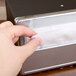 A hand using a black Vollrath Minifold napkin dispenser with a chrome faceplate to dispense a white napkin.