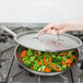 A hand holding a Vollrath stainless steel fry pan full of vegetables
