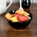 A black plastic swirl bowl filled with fruit on a table.