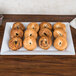 An American Metalcraft white melamine platter with bagels on it sitting on a table.