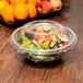 A clear plastic dome lid on a salad in a plastic bowl.