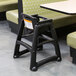 A black Rubbermaid restaurant high chair with wheels at a table.