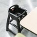 A black Rubbermaid high chair with wheels on a table.