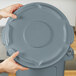 A person holding a grey Rubbermaid Brute trash can lid.