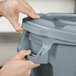 A person opening a Rubbermaid gray trash can lid.