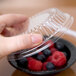 A person holding a clear Dart plastic container with a bowl of berries and a clear plastic dome lid.