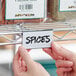 A hand using a Regency shelf label holder to label spices on a shelf.