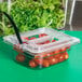 A Carlisle clear plastic container lid with tomatoes and lettuce inside on a green counter.