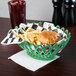 A forest green oval plastic fast food basket filled with a hamburger and fries on a table in a fast food restaurant.