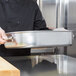 A chef holding a Vollrath aluminum roasting pan with handles.