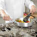 A chef in a white coat using a spatula to cook food in a Vollrath Wear-Ever saute pan.
